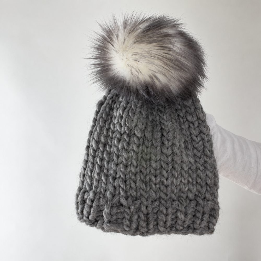 Charcoal grey chunky knitted beanie with a large faux fur pompom, from the Easy Beanie Knitting Pattern by Brome Fields