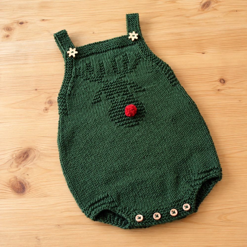 Green knitted baby romper with a reindeer face, red pompom nose and wooden buttons, from the Rodolph pattern by Filipa Carneiro