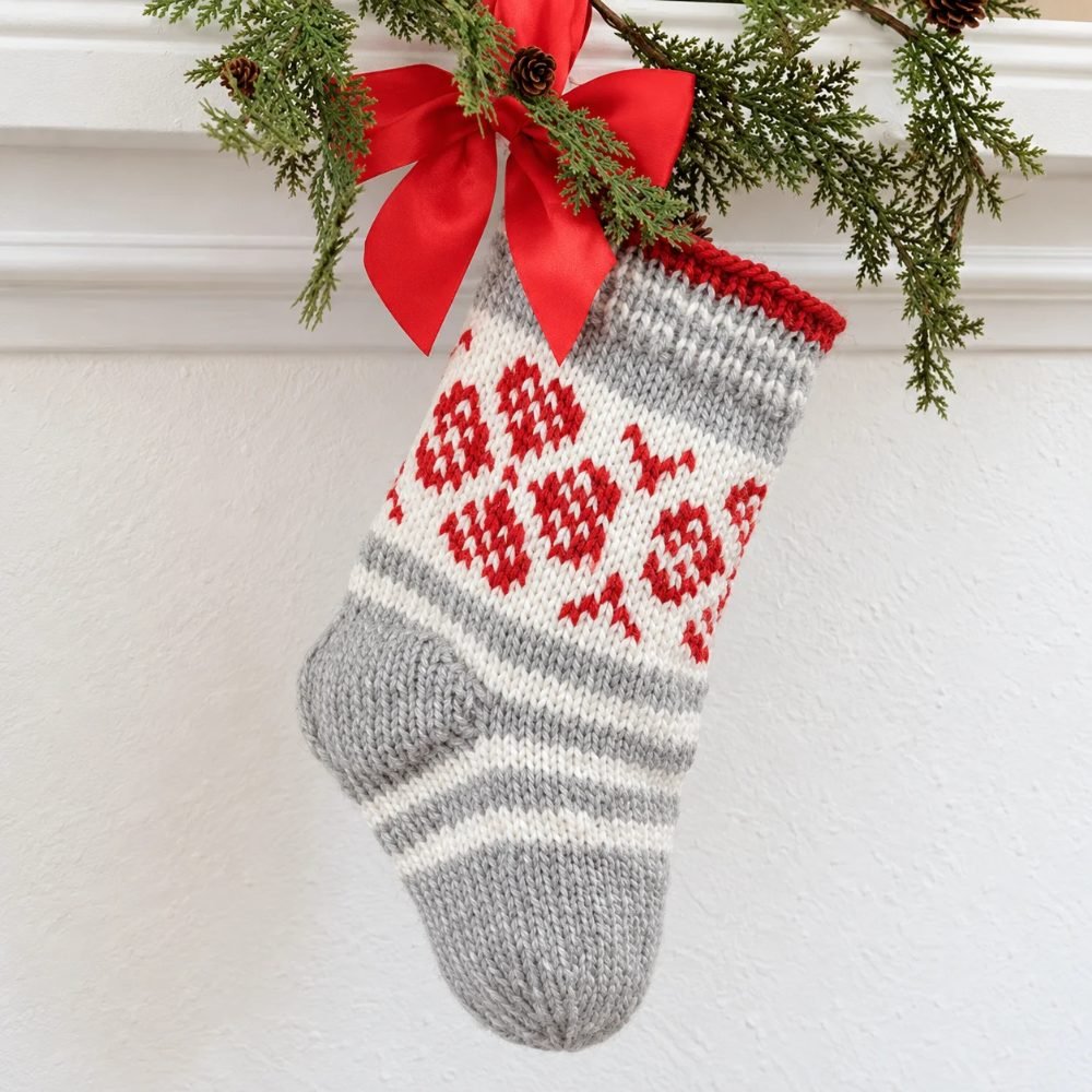 Grey and white knitted Christmas stocking with red Nordic hearts and stripes under a red bow, DROPS Christmas Flower Stocking
