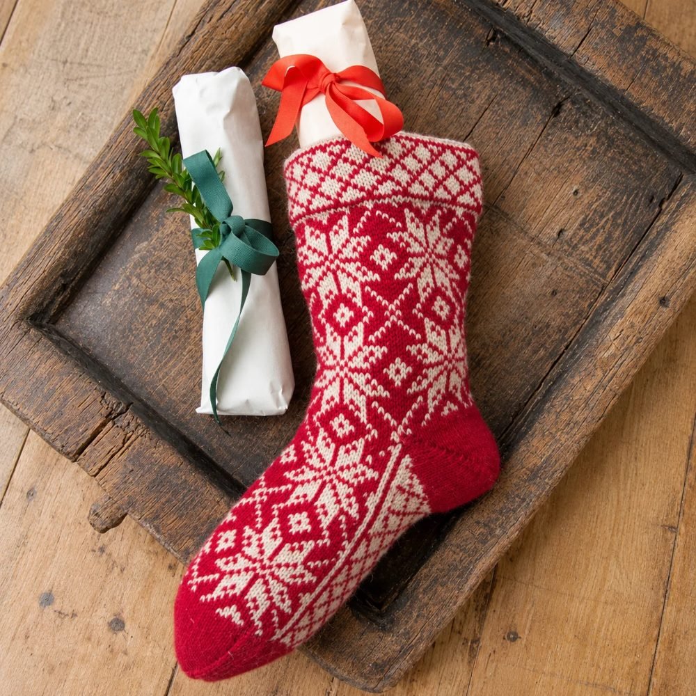 Red and white Norwegian-pattern knitted Christmas stocking in a wooden tray with wrapped gifts, DROPS Nick's Sock