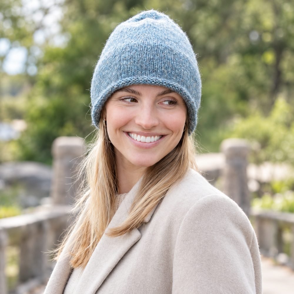 Blue grey knitted hat with a double folded brim worn outdoors by the water, DROPS Washed Tide Hat