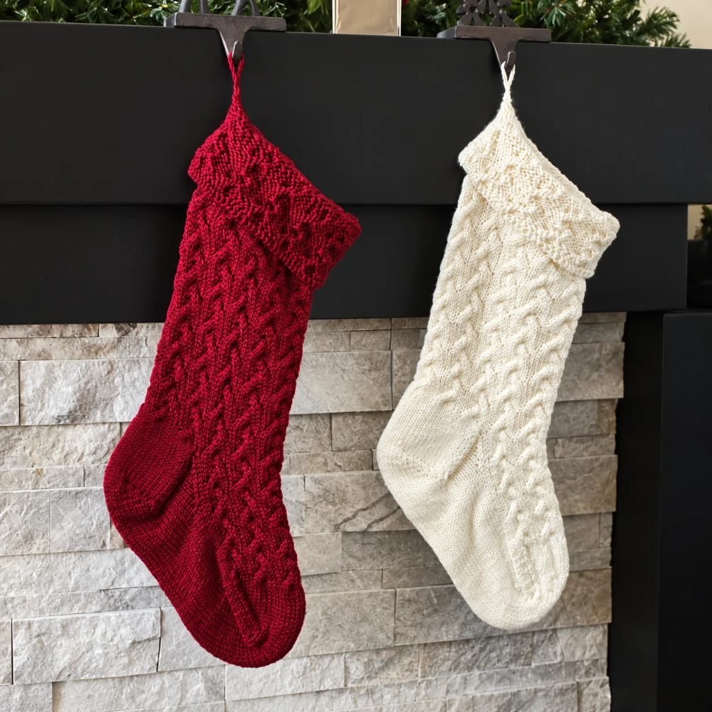Red and cream cable knitted Christmas stockings hanging from a mantel, from Leelee Knits